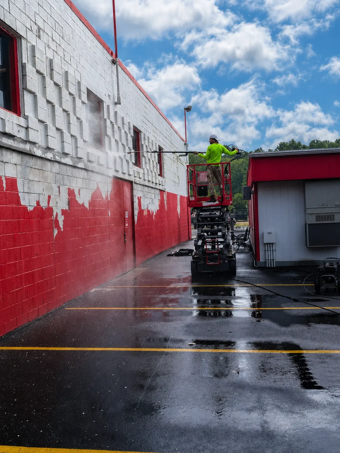 Worker on a scissor lift pressure washing a red and white commercial building