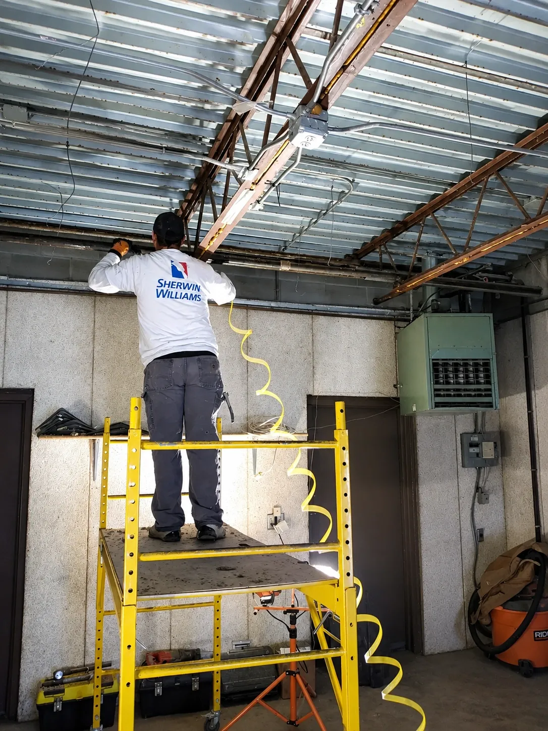 Worker on rolling scaffold preparing the ceiling of an industrial garage