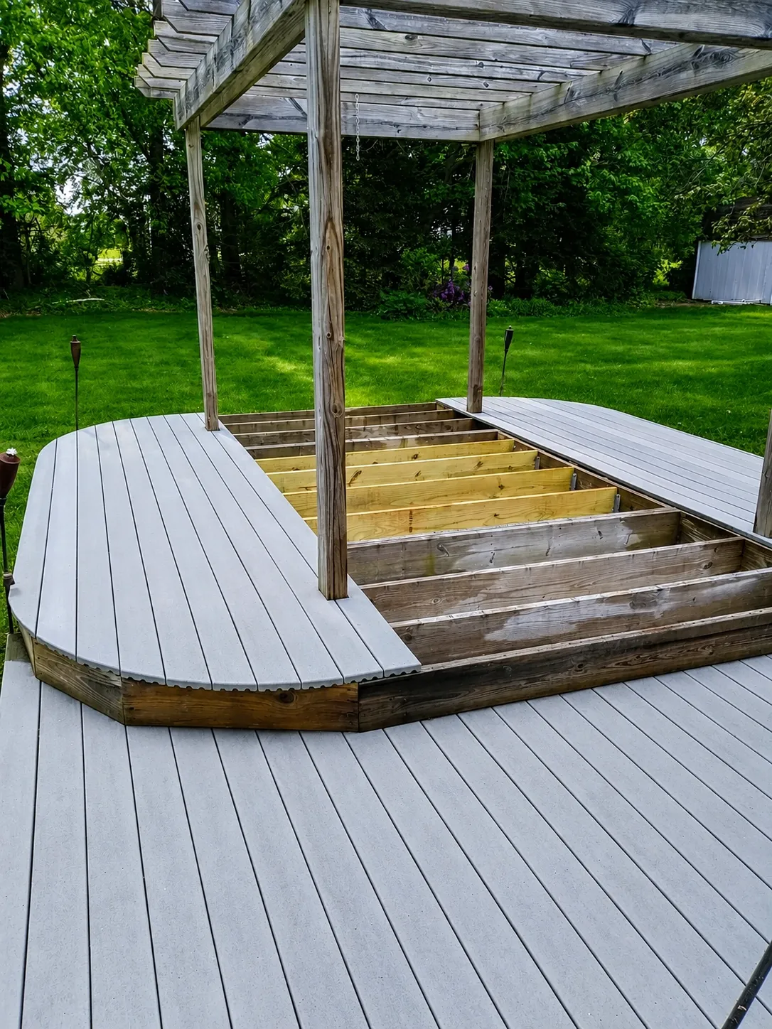 Gray composite deck boards being installed under a wood pergola