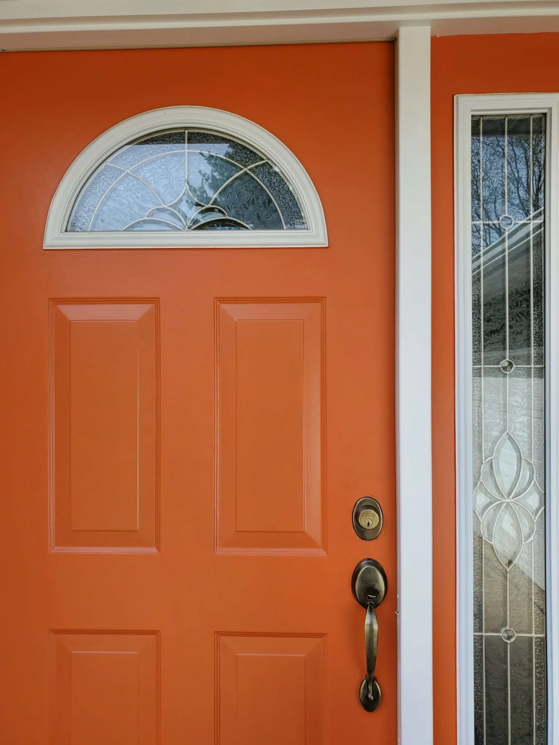 Freshly painted orange front door with white trim and a fan-light window
