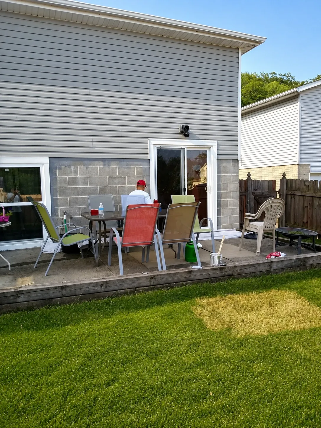 Painter working on the rear siding of a gray home above a backyard patio