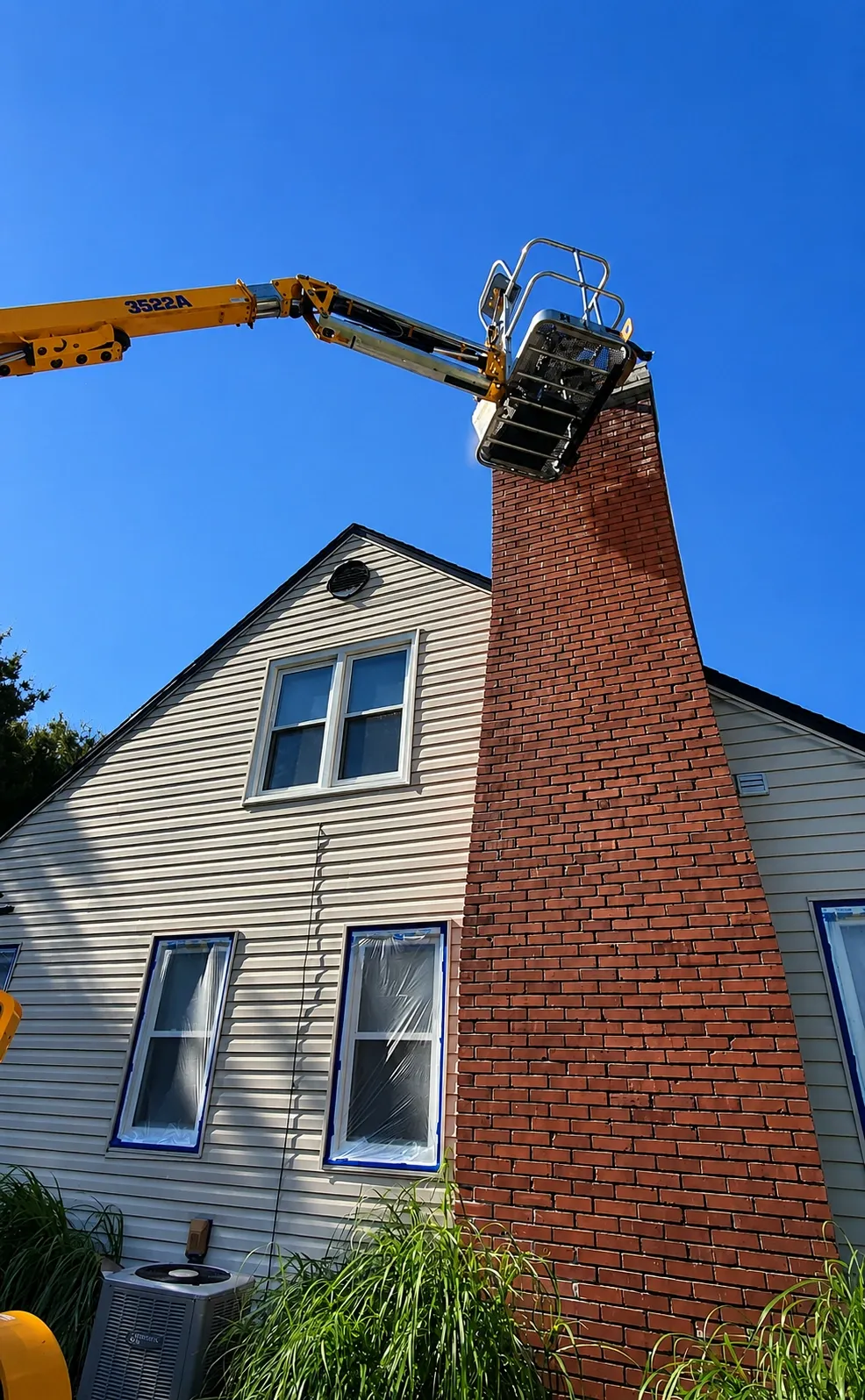 Boom lift reaching a brick chimney with masked windows on the siding below
