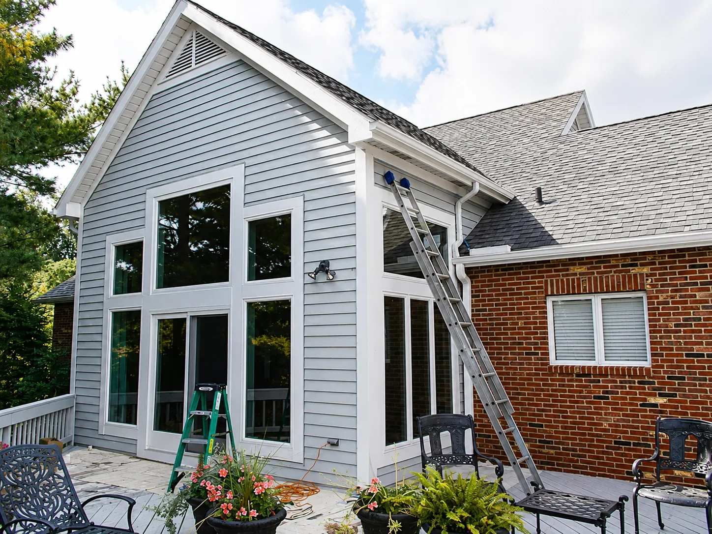 Residential exterior painting project with ladders and masking visible