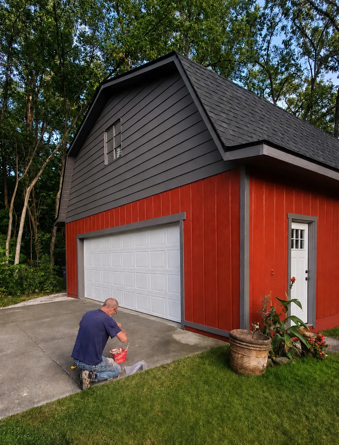 Red barn-style garage with a dark gambrel roof and white overhead door