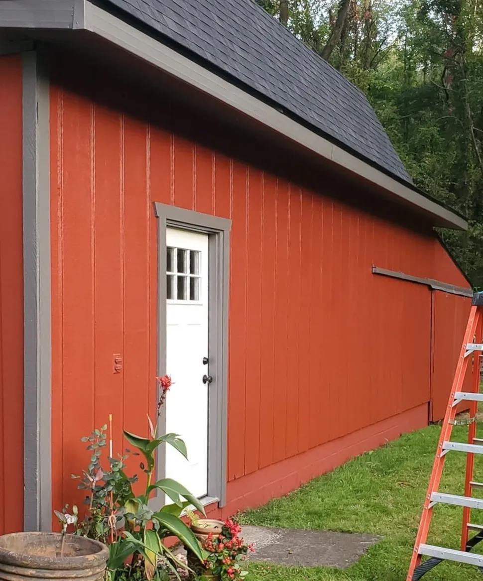 Red board-and-batten outbuilding with gray trim and a white door