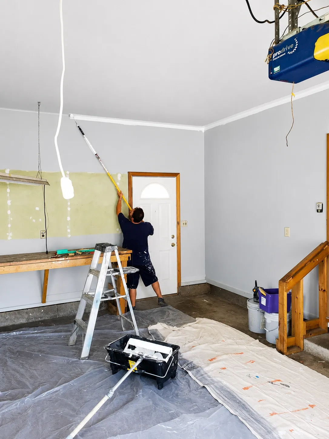 Painter rolling a garage interior wall with dropcloths protecting the floor