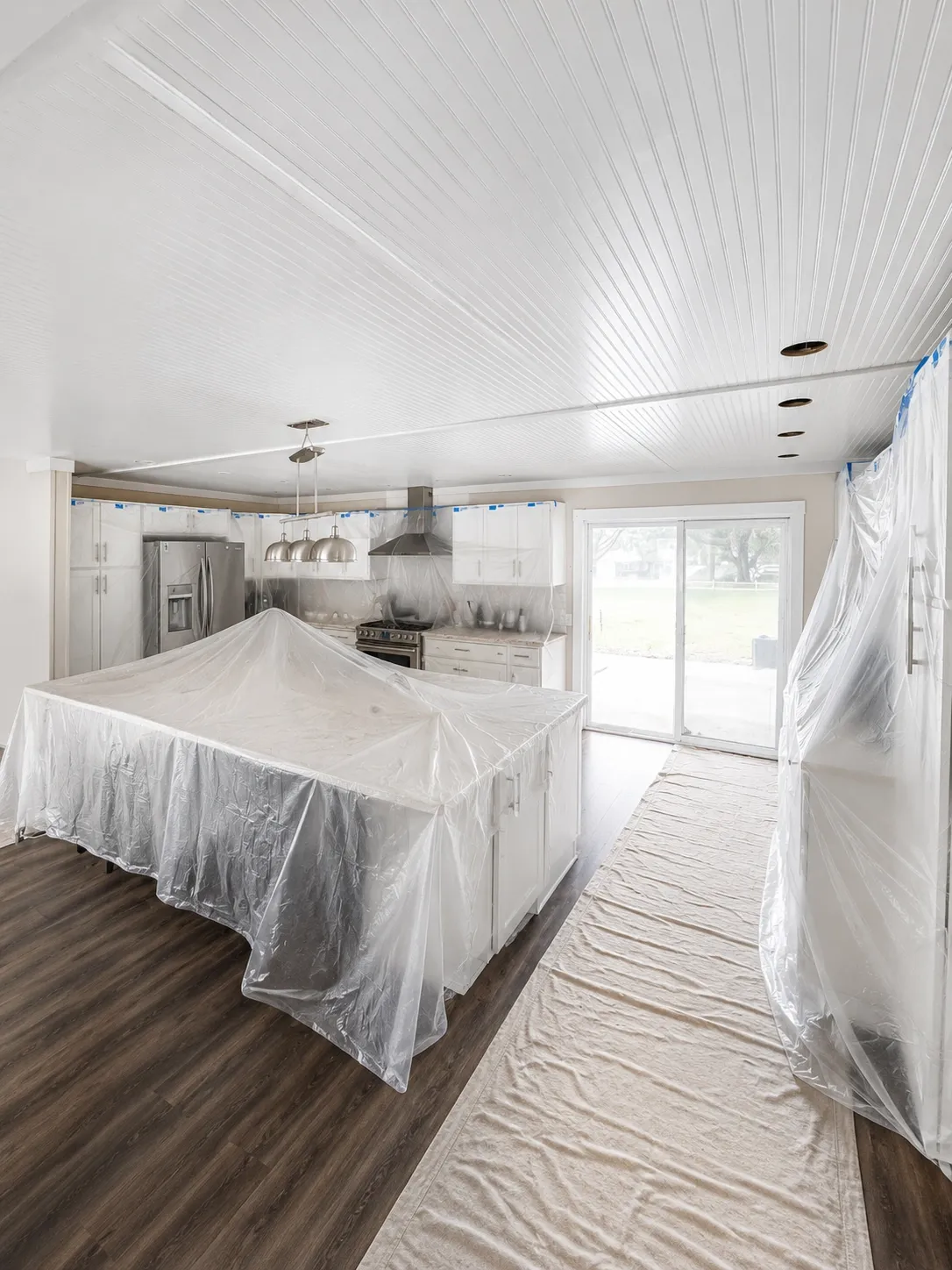 Kitchen island and cabinets covered in plastic sheeting with dropcloths and blue tape