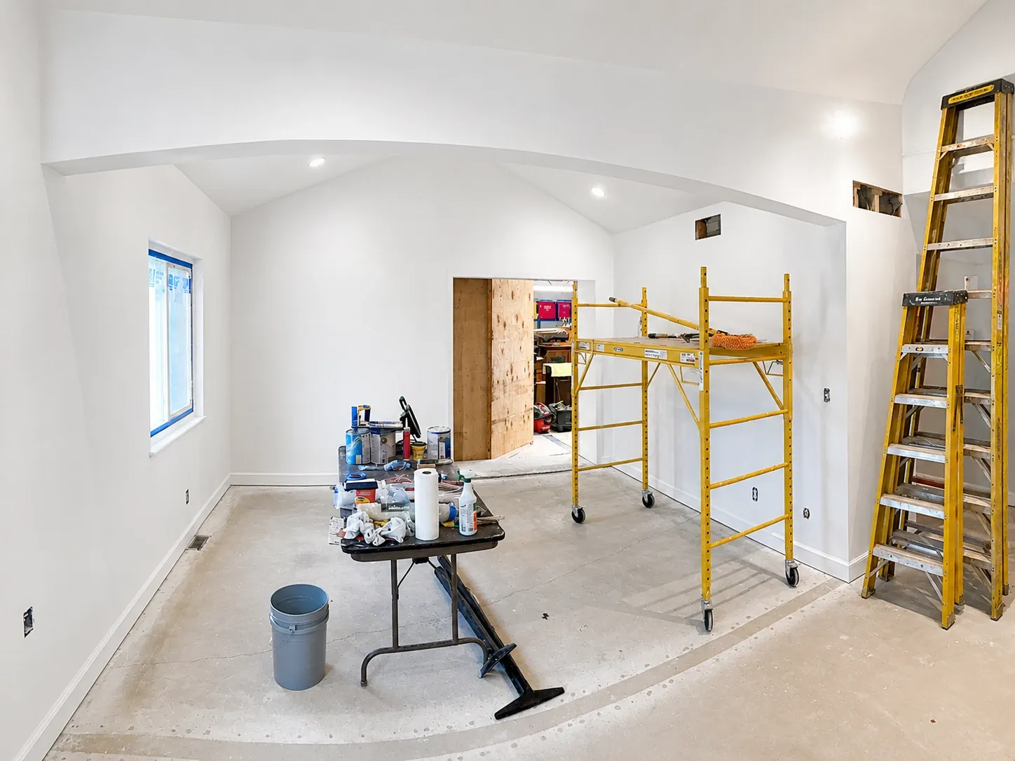 Interior painting project setup with ladders, scaffold, and paint supplies