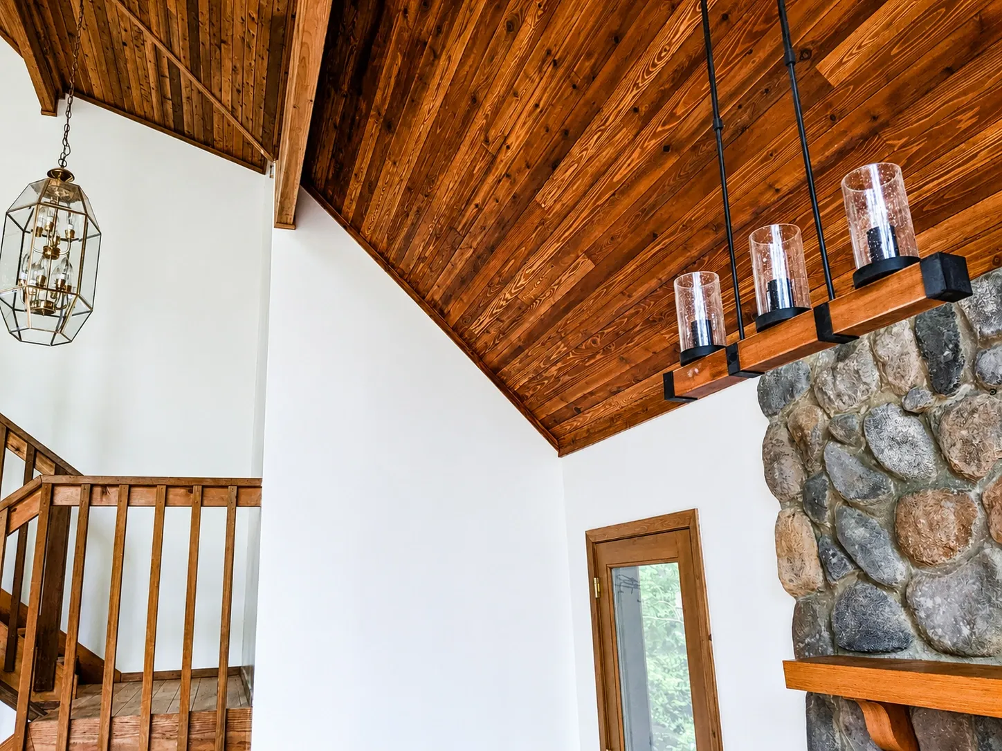 Vaulted interior with stained wood ceiling, white walls, and river rock chimney