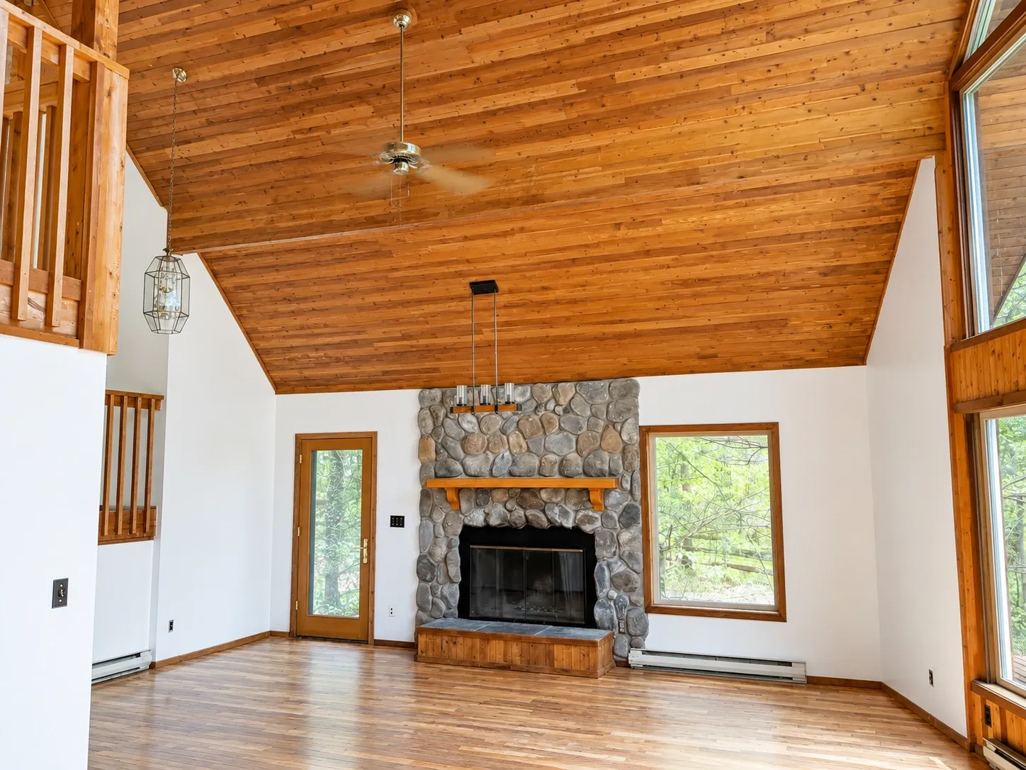 Bright residential interior with white walls, stained wood ceiling, and stone fireplace