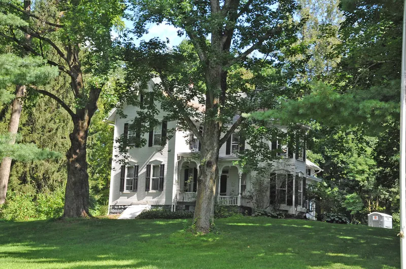The white Hartong farmhouse in Green, with its detailed porch shaded by mature trees.